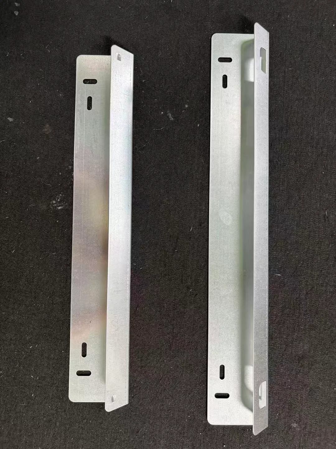 Two actual folded metal mounting plates with elongated fixing slots